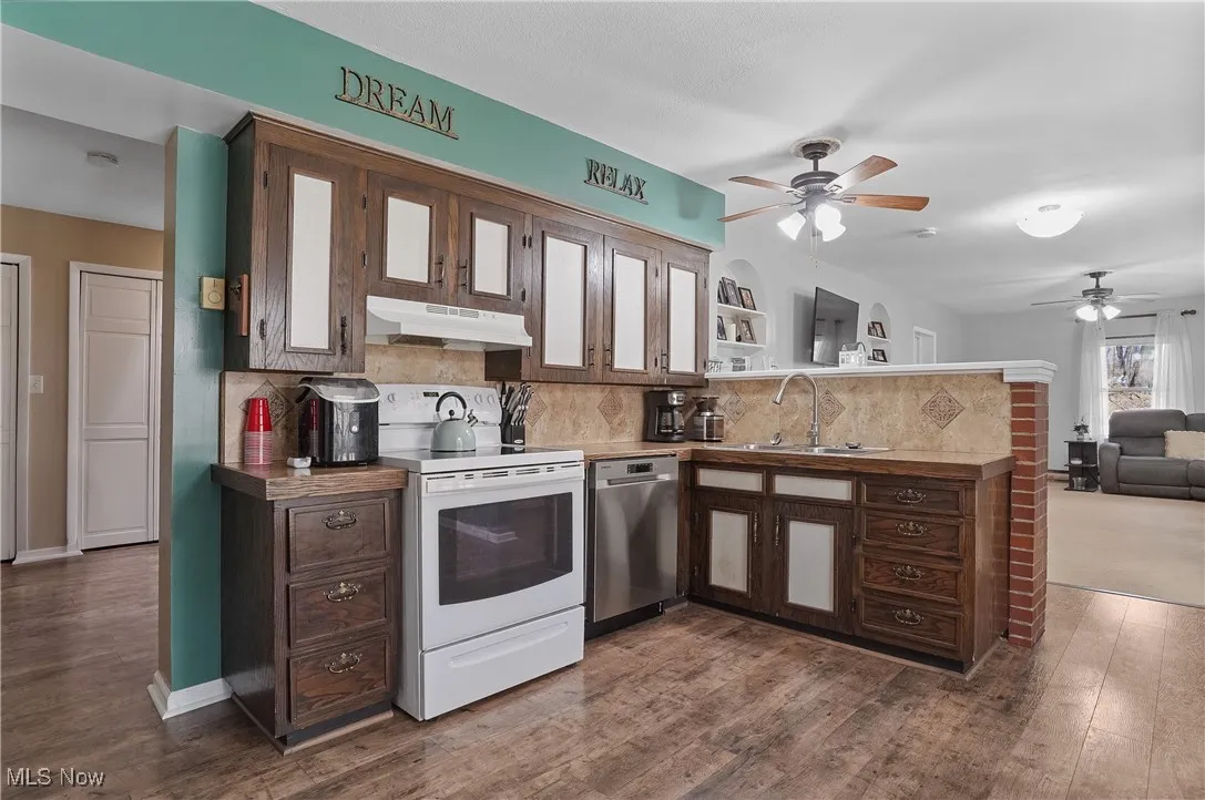 Kitchen with a peninsula, under cabinet range hood, electric stove, a sink, and stainless steel dishwasher