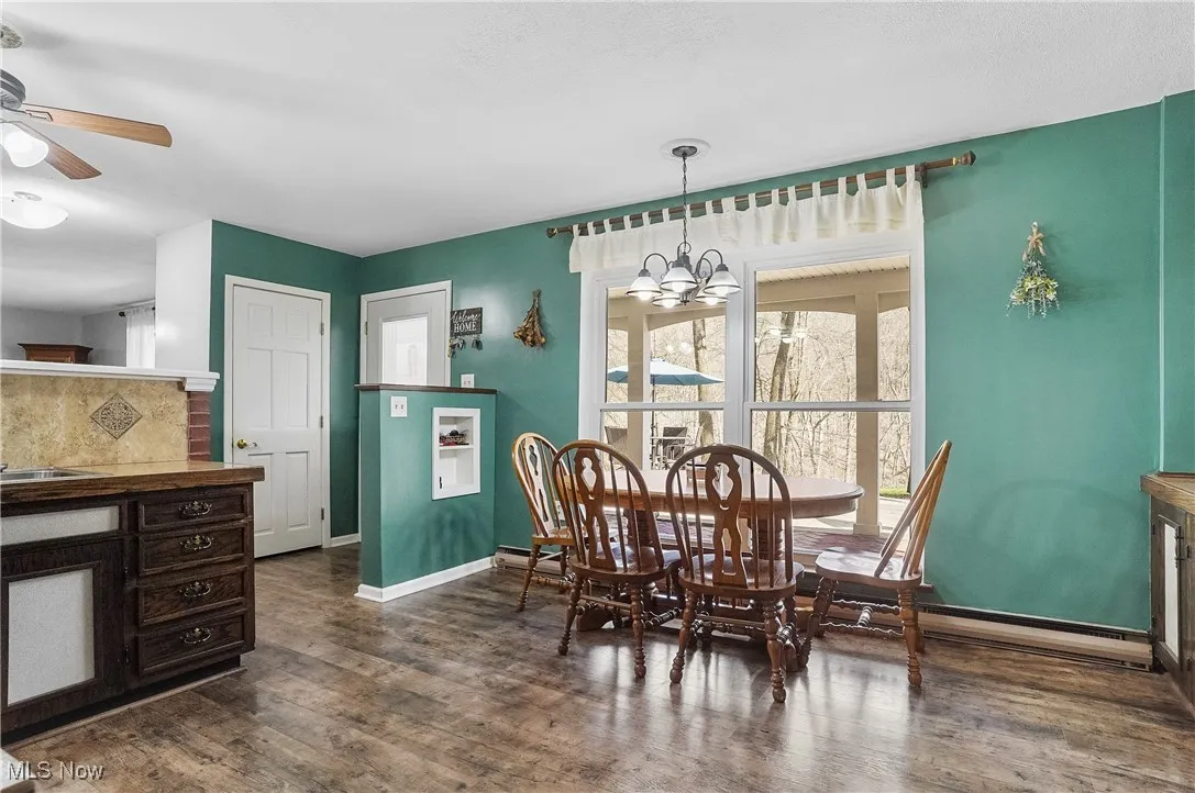 Dining room featuring dark wood-type flooring, baseboards, and ceiling fan with notable chandelier