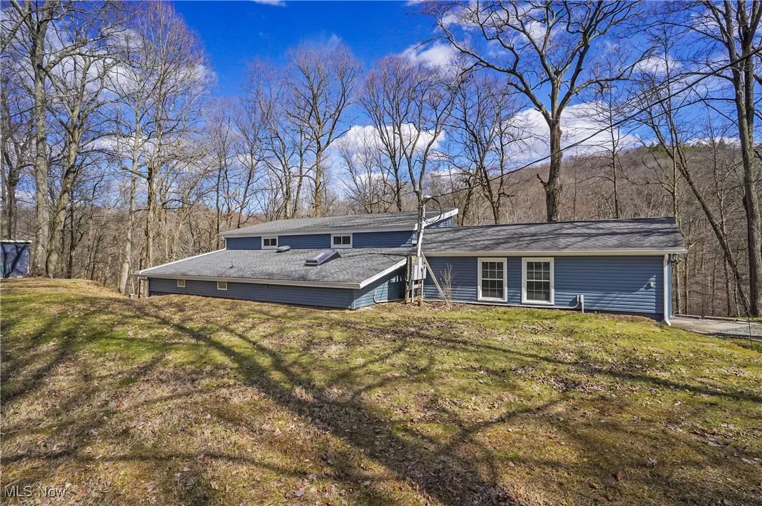 Rear view of house featuring a lawn and a forest view