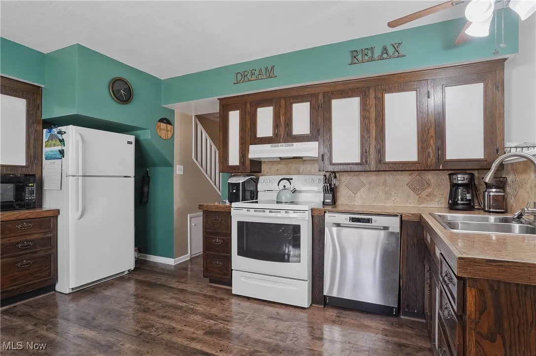 Kitchen with white appliances, tasteful backsplash, under cabinet range hood, and a sink