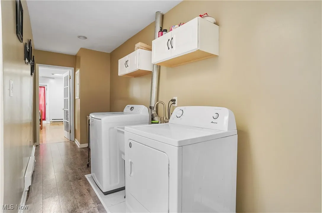 Washroom with washer and clothes dryer, a baseboard heating unit, baseboards, light wood finished floors, and cabinet space