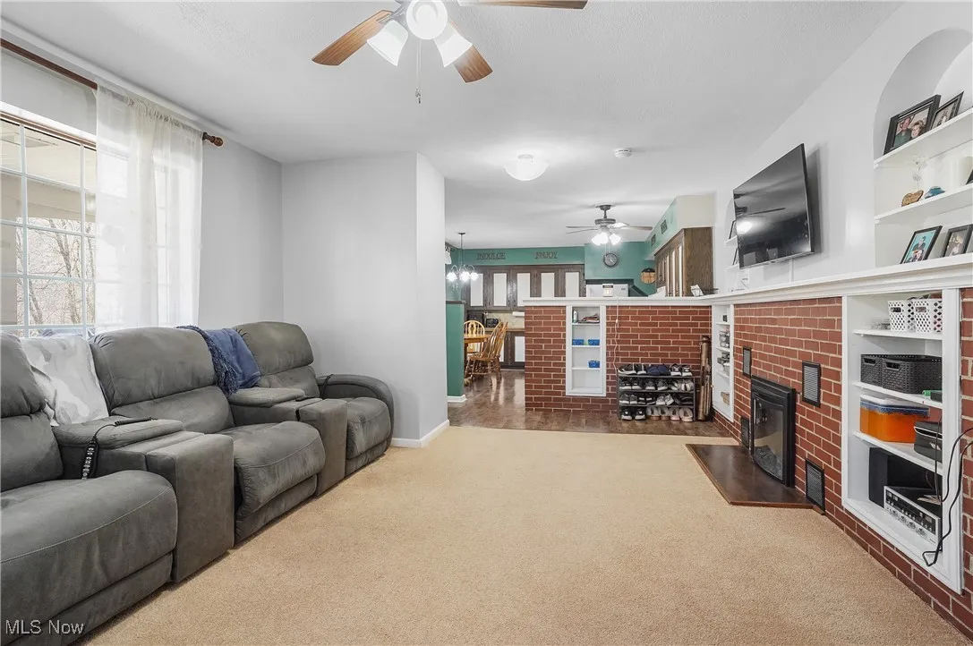 Carpeted living area featuring a fireplace and ceiling fan