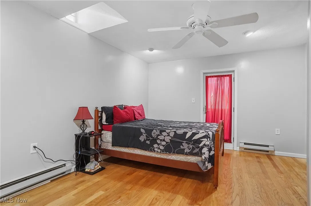 Bedroom with a baseboard radiator, wood finished floors, a skylight, and a ceiling fan