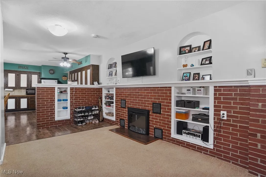 Living area with a brick fireplace, built in features, carpet, and ceiling fan