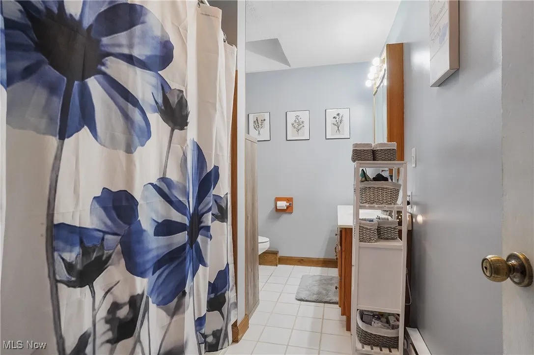 Bathroom with baseboards, toilet, vanity, a shower with curtain, and tile patterned flooring