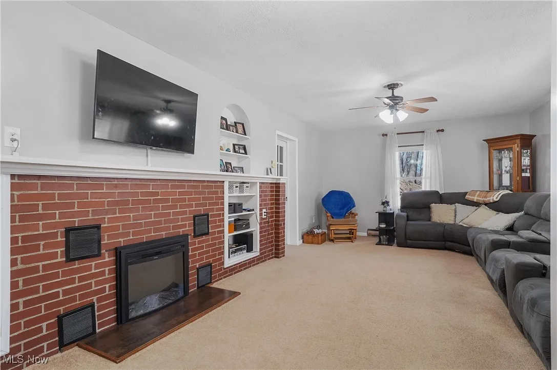 Living room featuring built in shelves, a ceiling fan, a brick fireplace, visible vents, and carpet