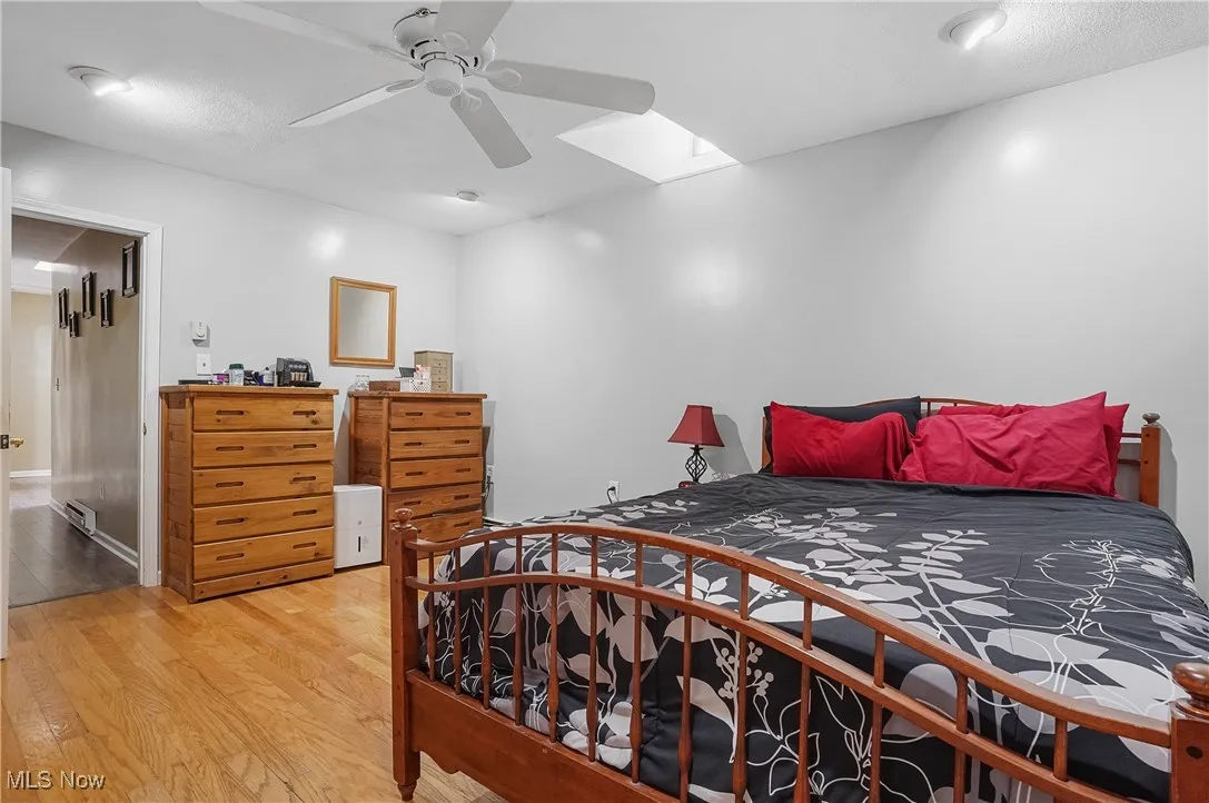 Bedroom with wood finished floors, a skylight, and a ceiling fan