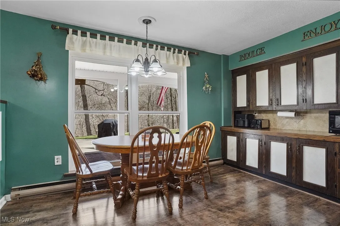 Dining room with baseboards, dark wood-style flooring, a wealth of natural light, and an inviting chandelier