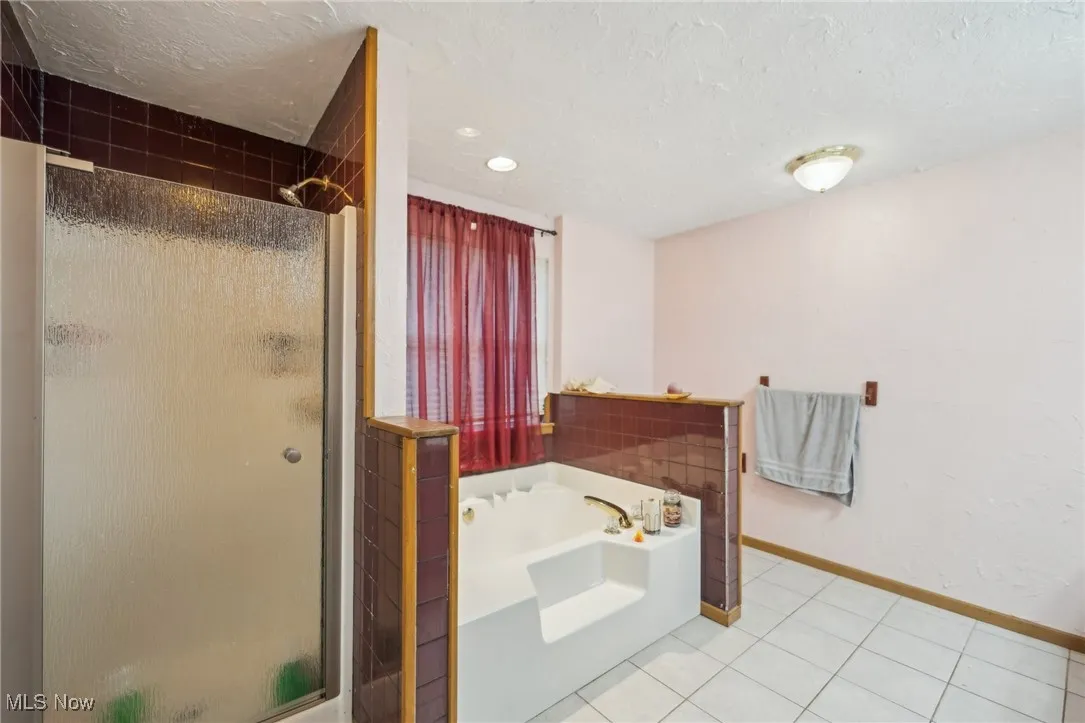 Full bath featuring tile patterned flooring, a bath, a textured ceiling, and a shower stall