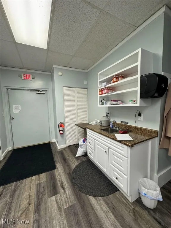 Kitchenette with a sink, open shelves, dark wood-style flooring, white cabinets, and a drop ceiling