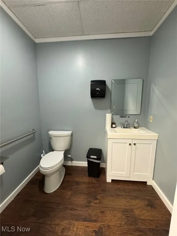 Half bathroom with toilet, vanity, baseboards, and wood finished floors