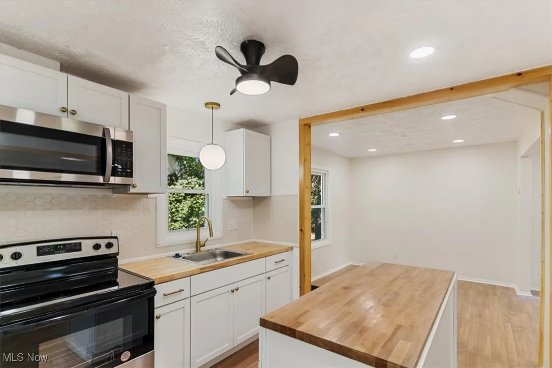 Kitchen featuring black / electric stove, white cabinetry, stainless steel microwave, light wood-type flooring, and recessed lighting