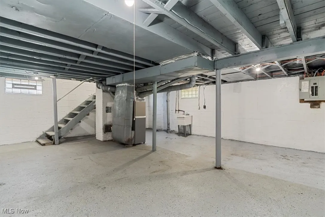 Basement with stairway, heating unit, and electric panel