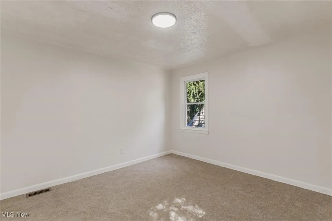 Carpeted spare room with a textured ceiling and baseboards