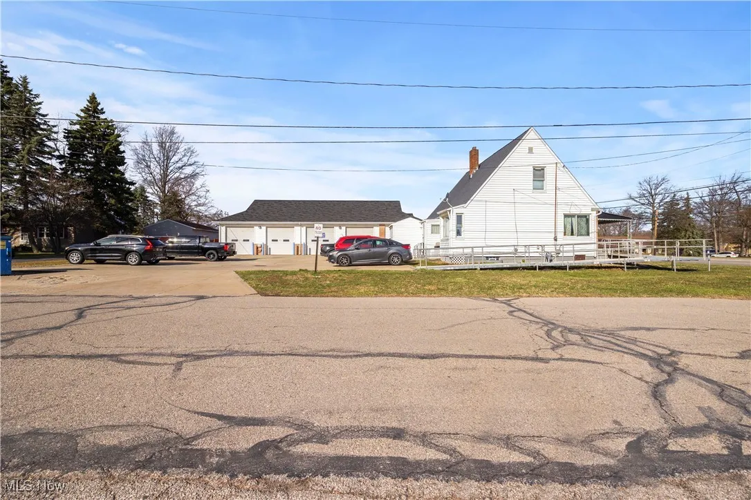 View of front facade featuring a chimney, a garage, concrete driveway, a front lawn, and an outbuilding