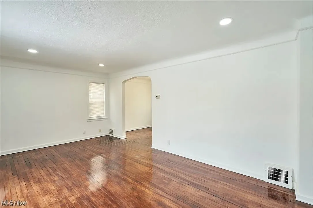 Empty room with a textured ceiling, visible vents, recessed lighting, arched walkways, and wood-type flooring