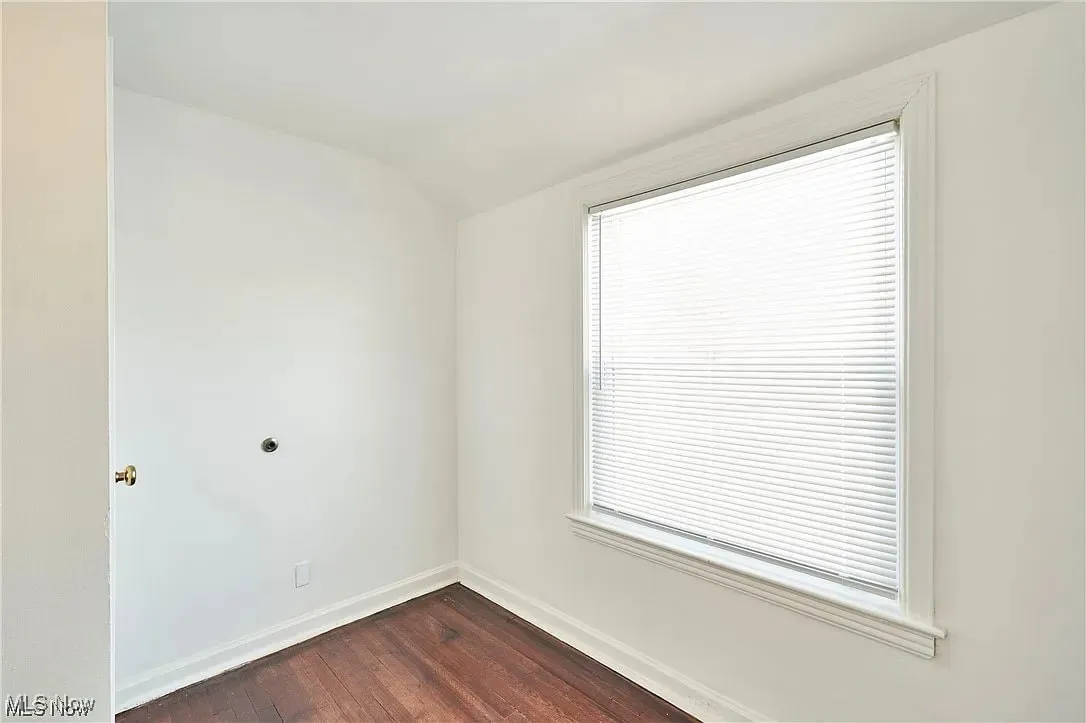 Spare room featuring dark wood-style floors, baseboards, and lofted ceiling