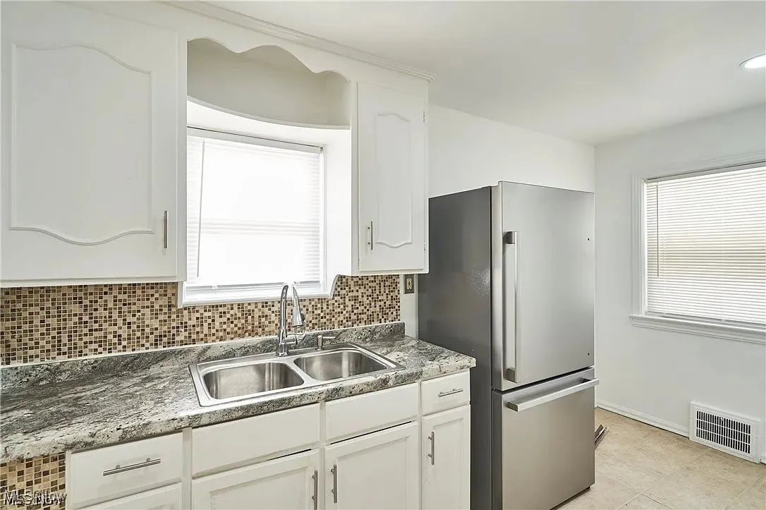Kitchen with backsplash, a sink, freestanding refrigerator, white cabinetry, and visible vents