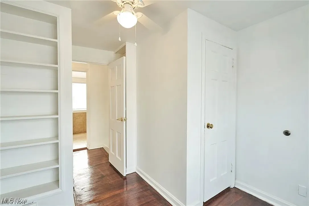 Corridor with dark wood-type flooring, baseboards, and built in shelves