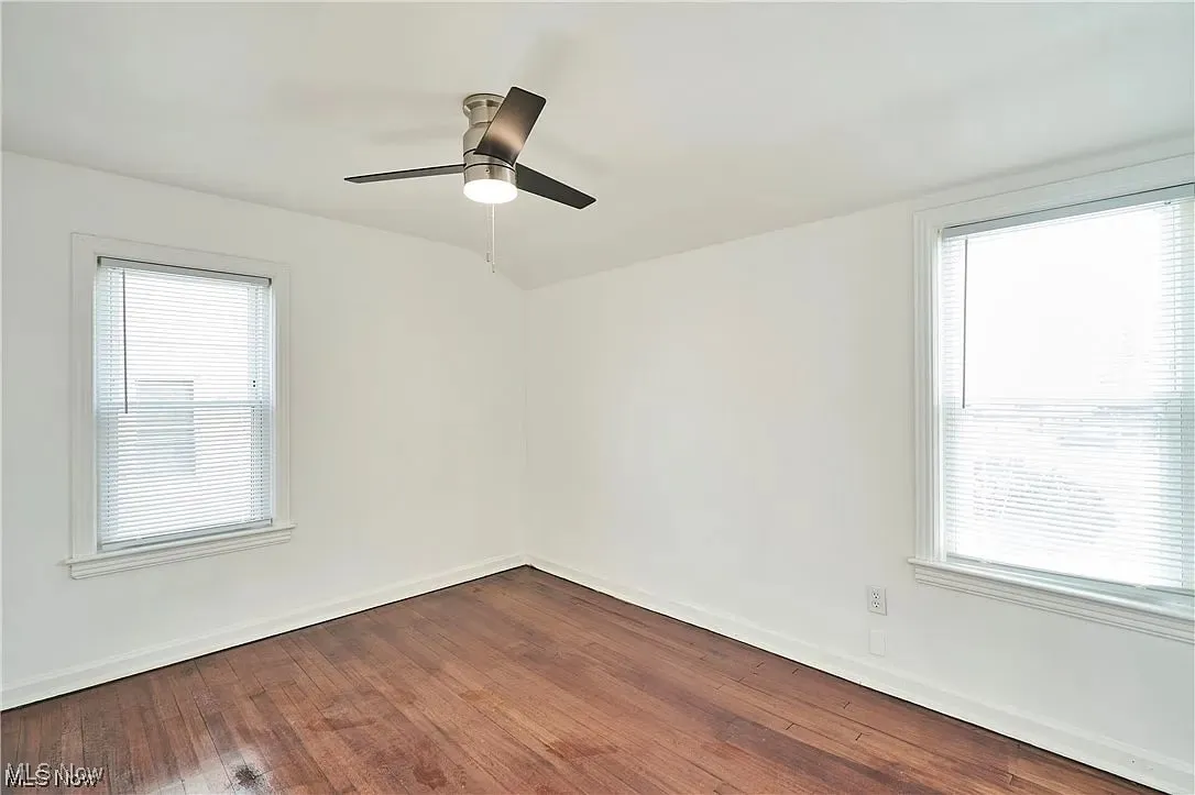 Unfurnished room featuring a ceiling fan, dark wood-type flooring, and baseboards