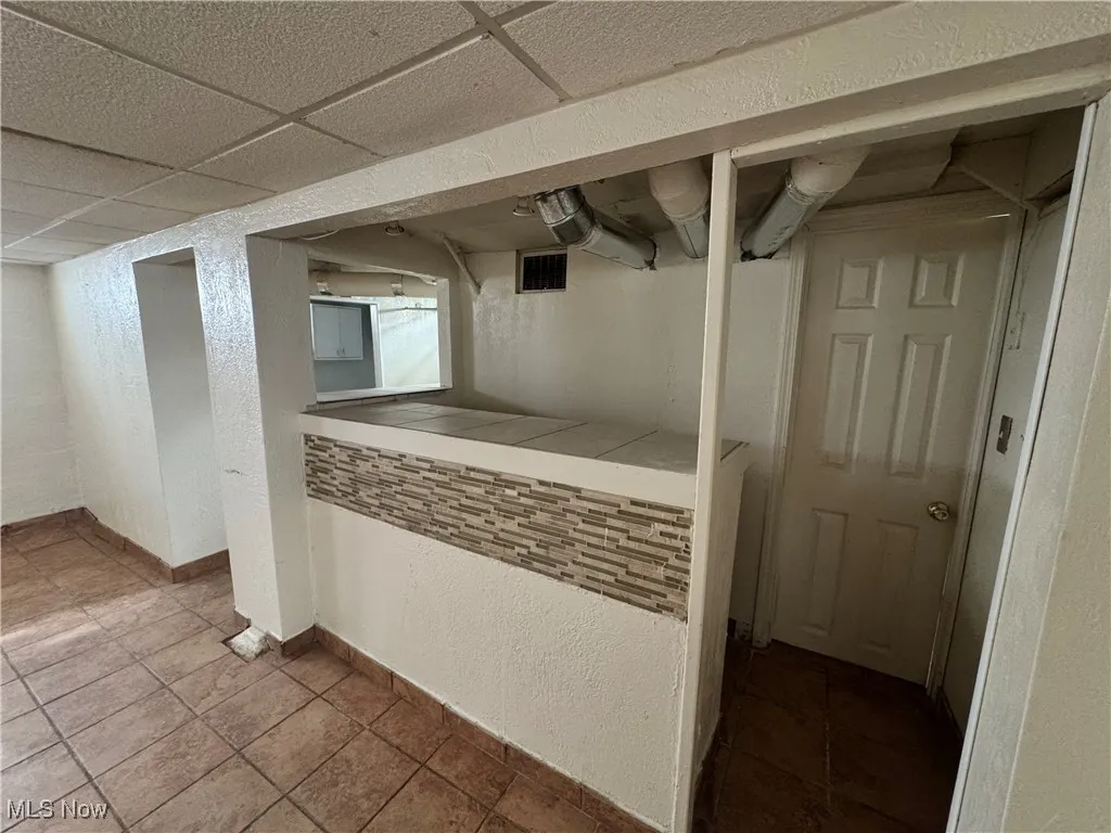 Finished basement with tile patterned flooring, a textured wall, baseboards, a drop ceiling, and visible vents