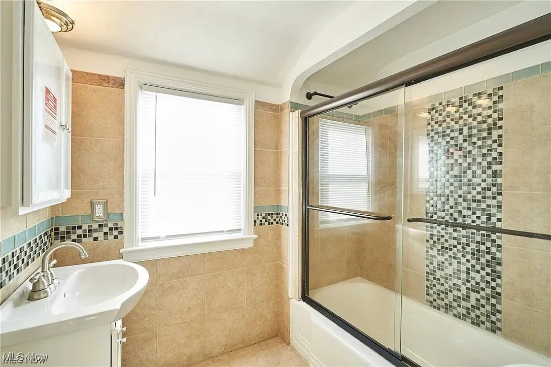 Bathroom with backsplash, shower / bath combination with glass door, tile walls, and vanity
