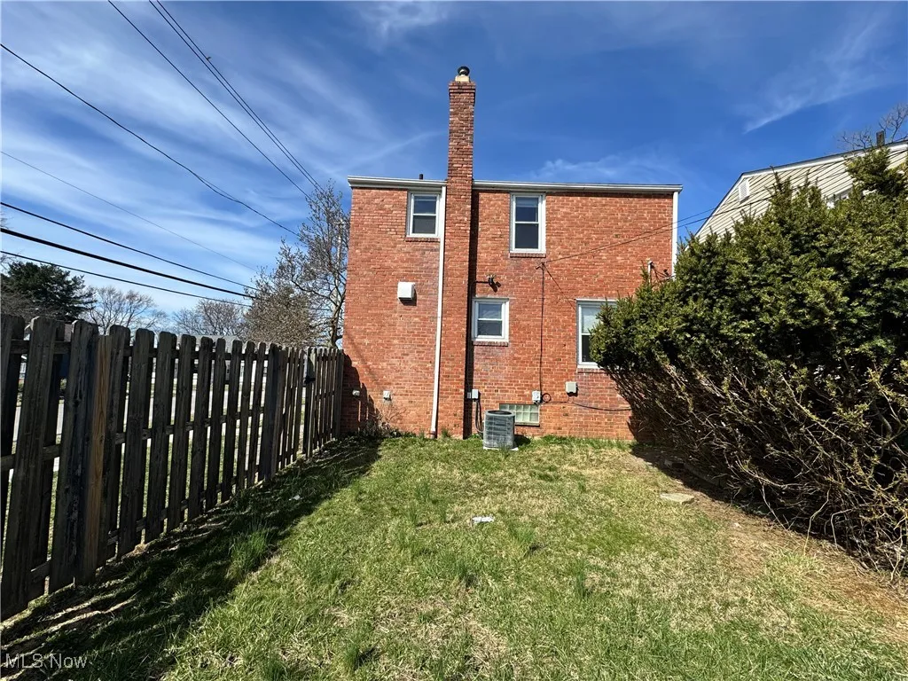 Rear view of house featuring a lawn, a chimney, fence, and brick siding