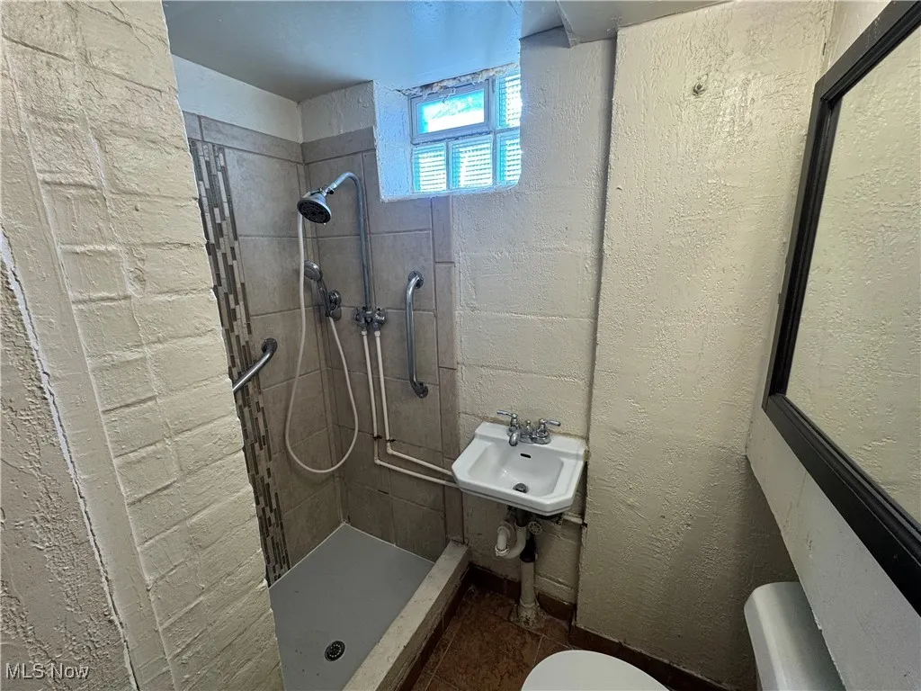 Basement Bathroom featuring a tile shower, toilet, and a sink