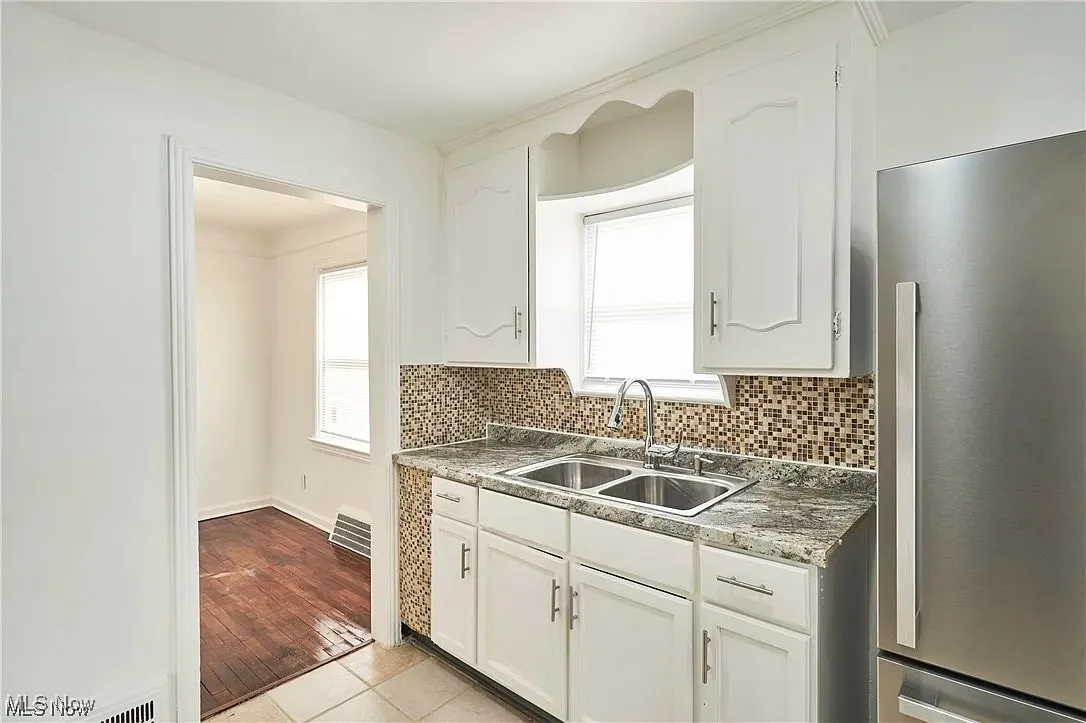 Kitchen featuring white cabinetry, tasteful backsplash, a sink, and freestanding refrigerator