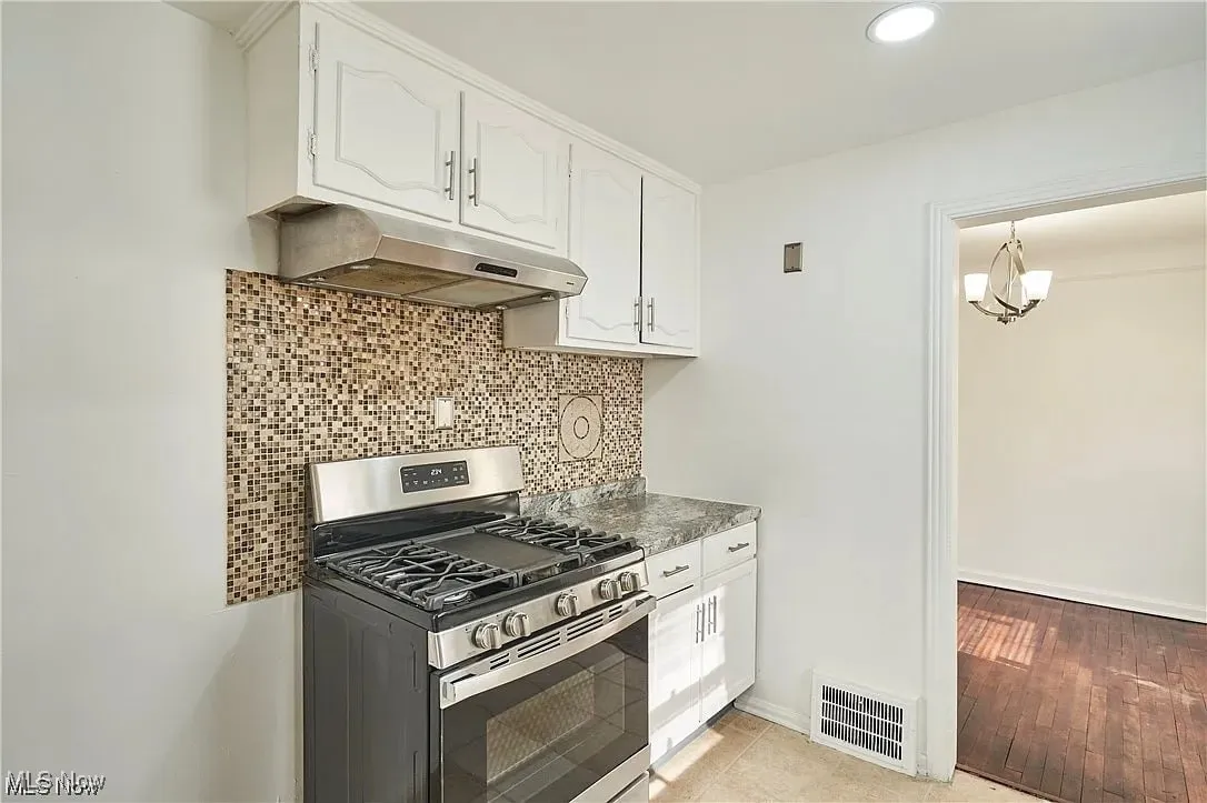 Kitchen featuring white cabinetry, under cabinet range hood, backsplash, stainless steel gas range, and visible vents