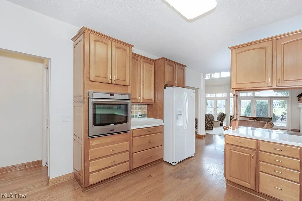 Kitchen with white fridge with ice dispenser, light wood-style flooring, stainless steel oven, and light brown cabinets