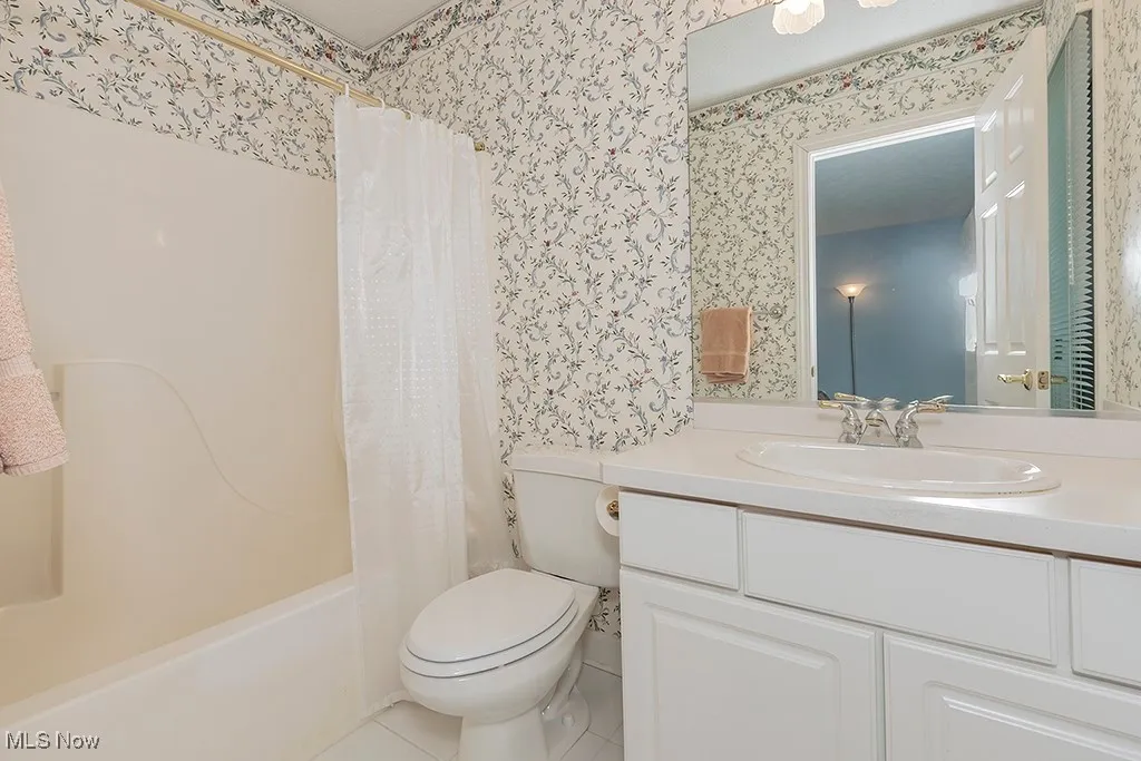Bathroom with tile patterned floors, toilet, shower / tub combo with curtain, vanity, and wallpapered walls