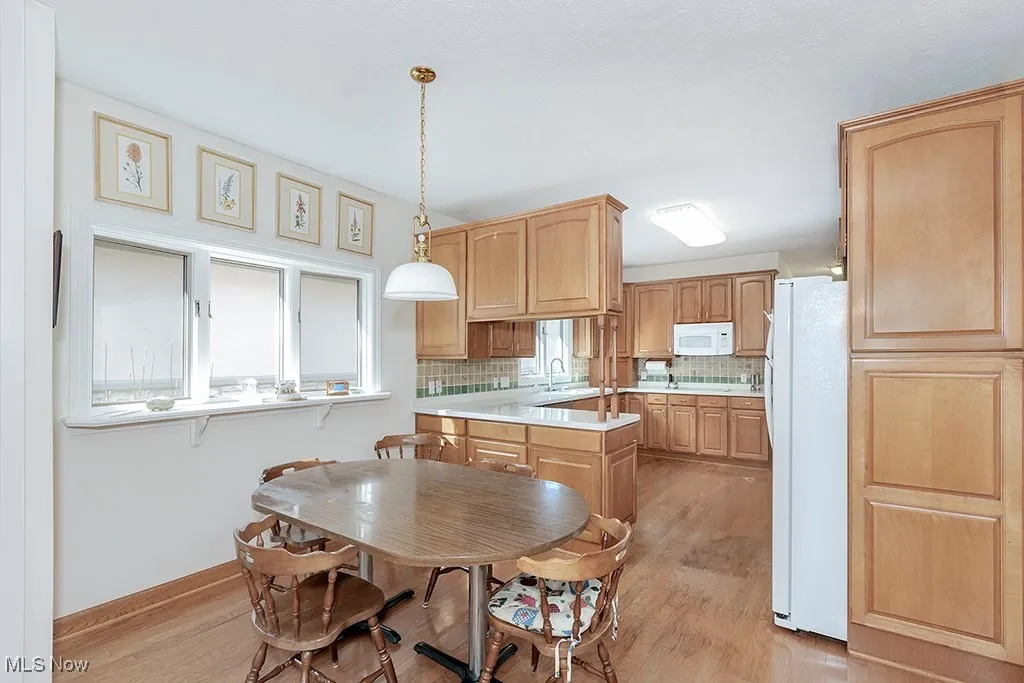 Kitchen featuring light wood-style floors, light countertops, backsplash, and white appliances