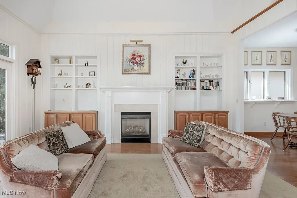 Living area featuring built in features, lofted ceiling, a fireplace, and wood finished floors