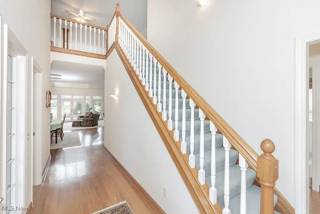 Staircase featuring baseboards, a high ceiling, wood finished floors, and a ceiling fan