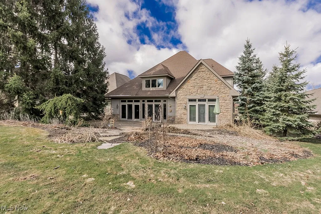 Rear view of house featuring a patio, stone siding, and a yard