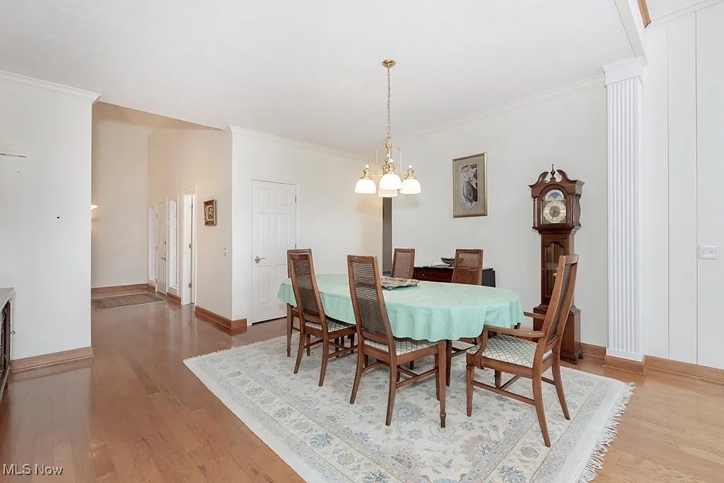 Dining space with baseboards, wood finished floors, an inviting chandelier, and crown molding