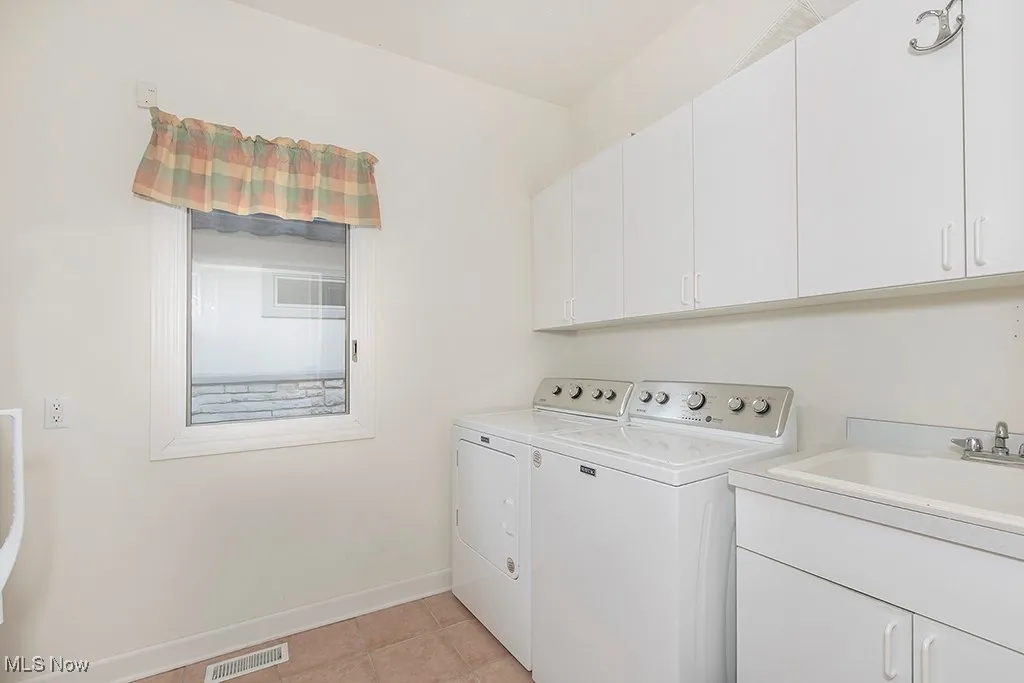 Clothes washing area with light tile patterned floors, baseboards, separate washer and dryer, a sink, and visible vents