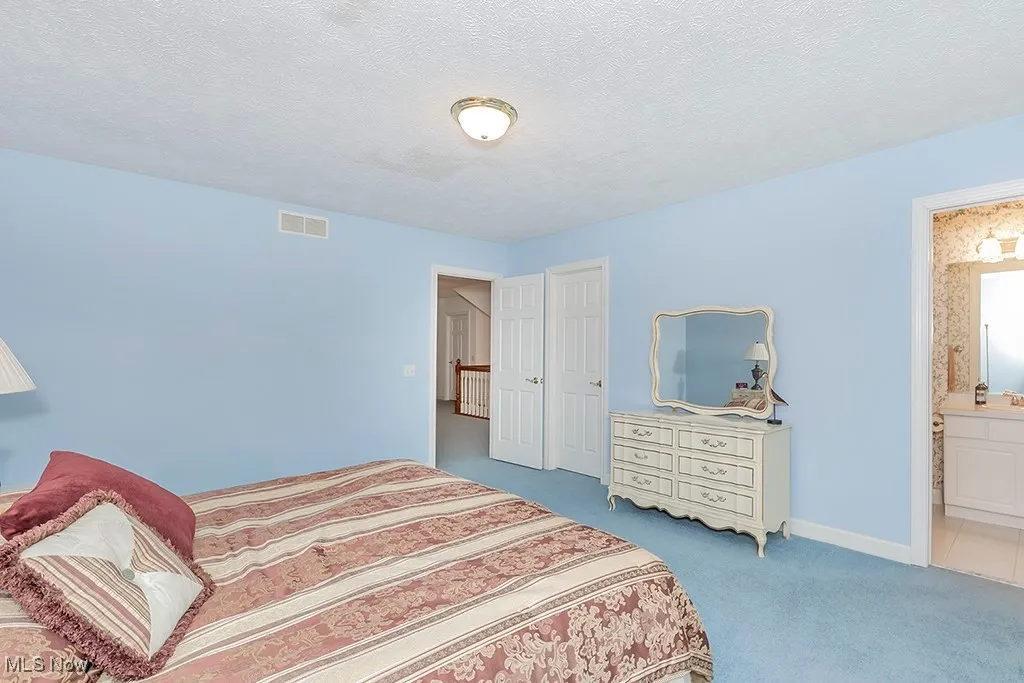 Bedroom with carpet flooring, a textured ceiling, ensuite bathroom, and visible vents
