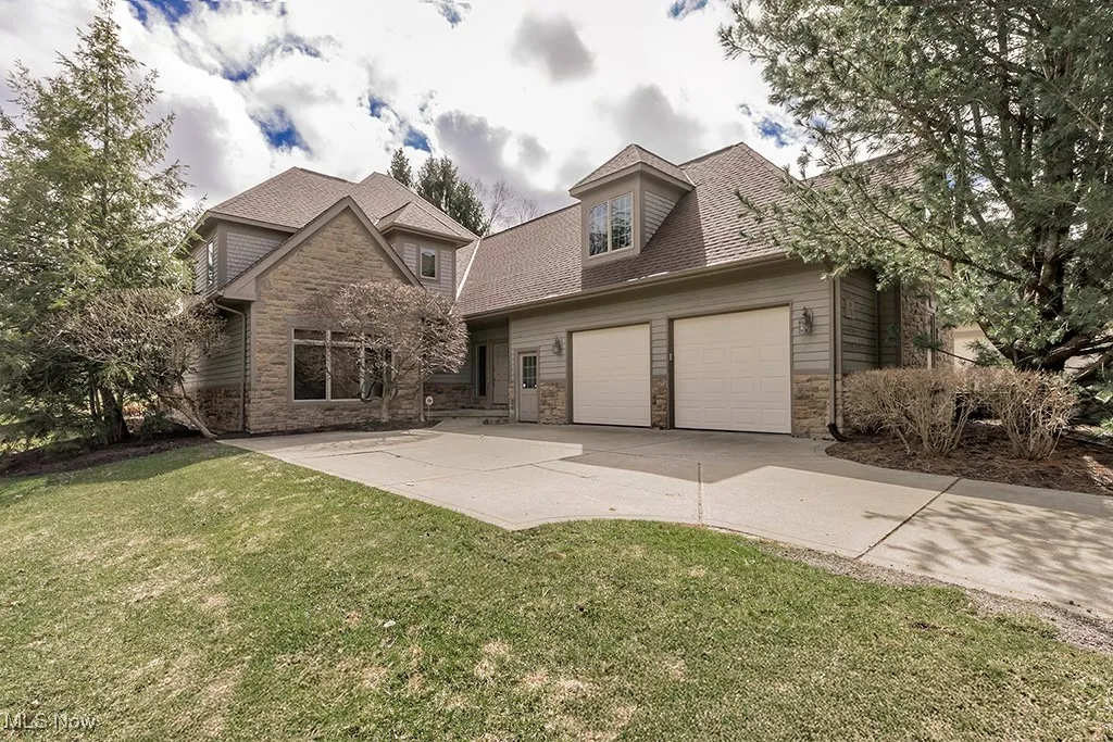 View of front of house with stone siding, a shingled roof, a garage, and a front lawn