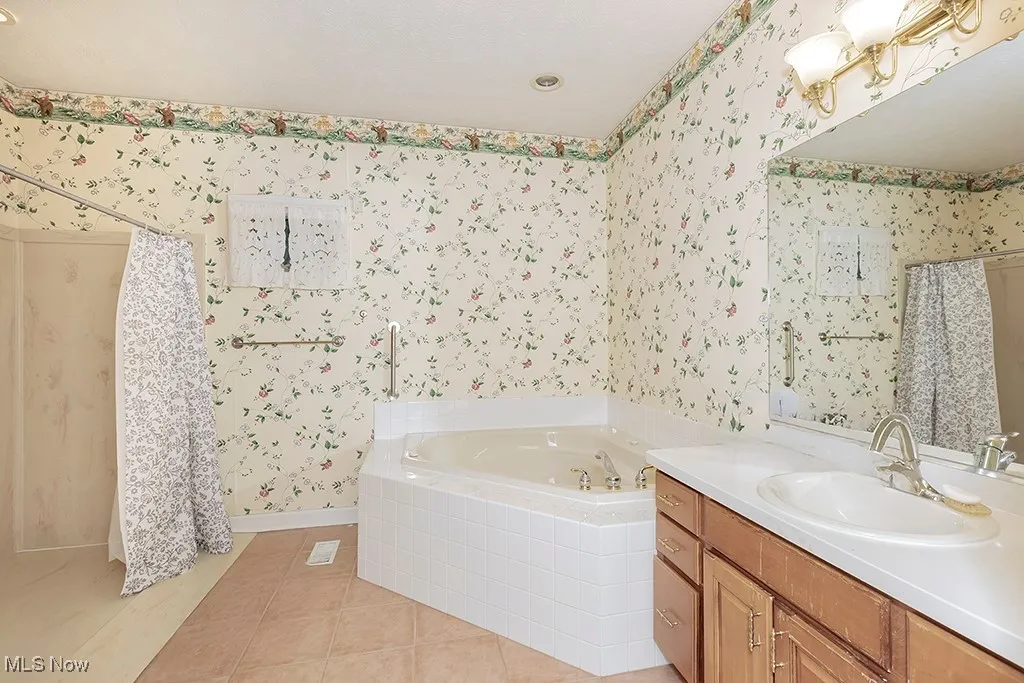 Full primary bathroom with vanity, wallpapered walls, tile patterned floors, a garden tub, and curtained shower