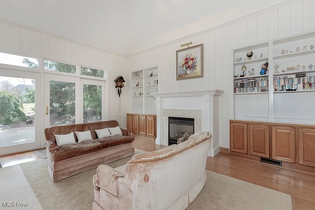 Living area featuring visible vents, built in shelves, light wood-style floors, a glass covered fireplace, and vaulted ceiling
