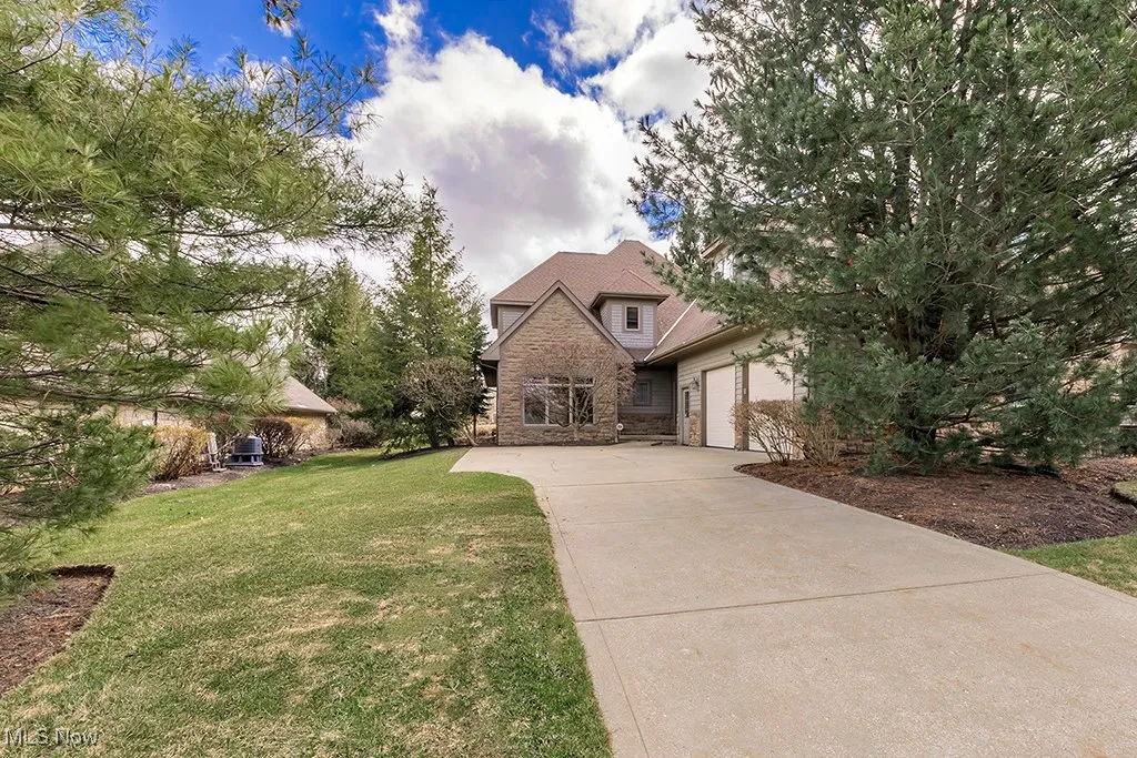 View of front of house featuring stone siding, driveway, a front lawn, and an attached garage