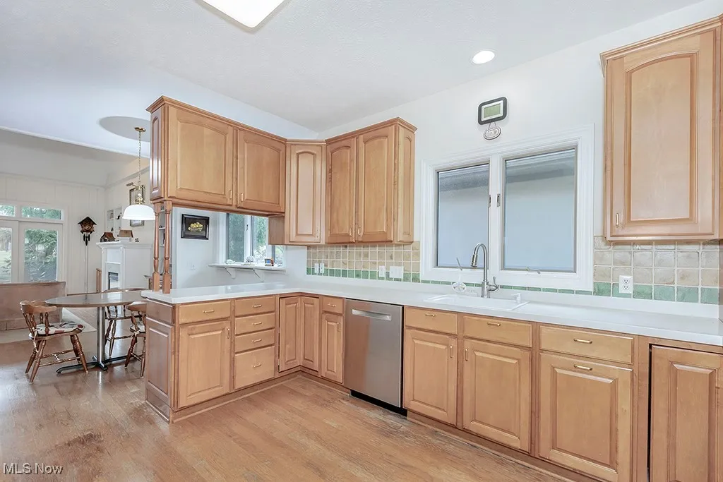 Kitchen with light wood-style flooring, dishwasher, a sink, backsplash, and light brown cabinetry
