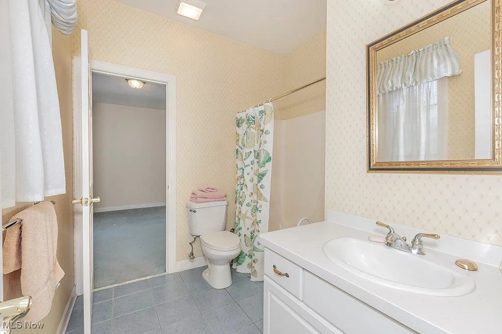 Full bath with tile patterned floors, toilet, vanity, baseboards, and wallpapered walls