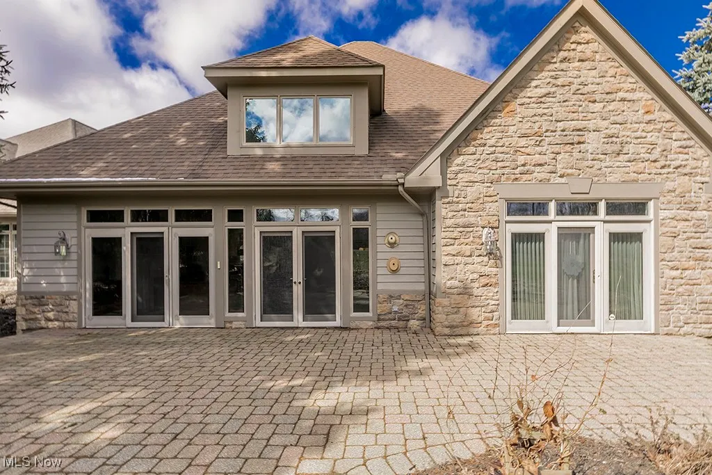 Rear view of property featuring stone siding, french doors, roof with shingles, and a patio