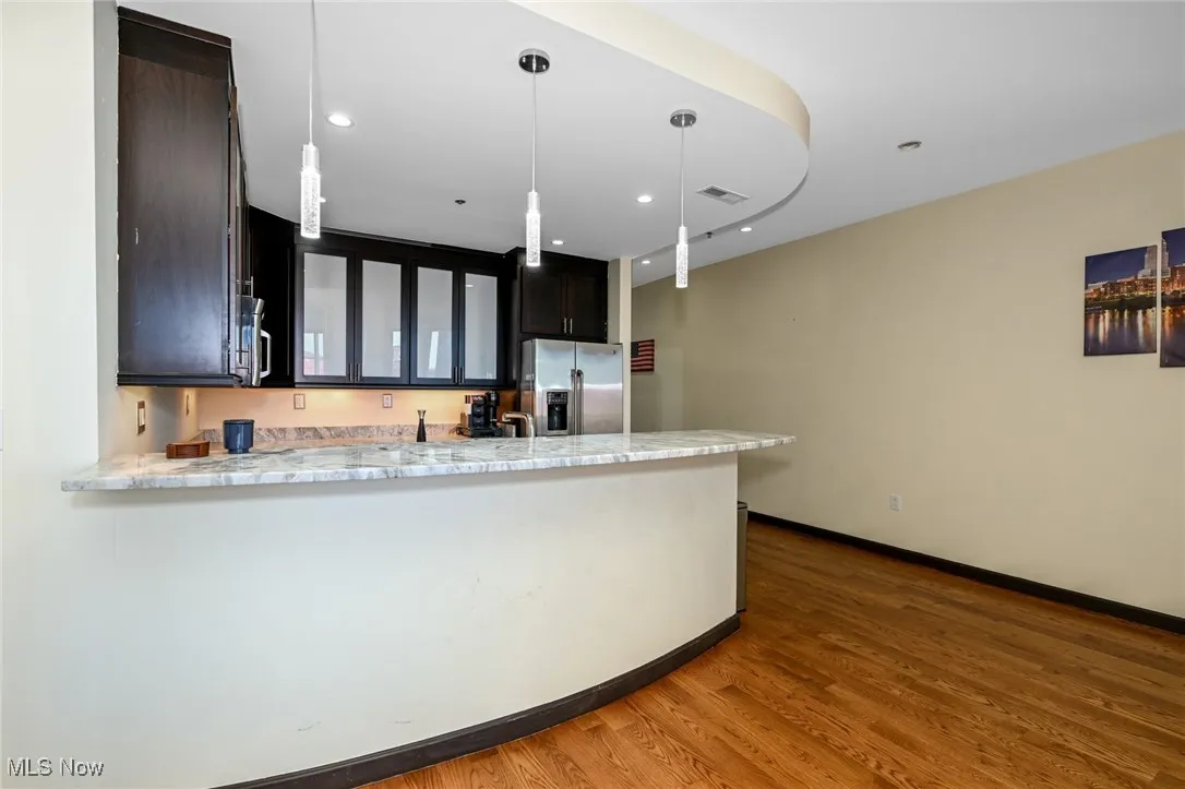 Kitchen featuring visible vents, a peninsula, wood finished floors, appliances with stainless steel finishes, and glass insert cabinets