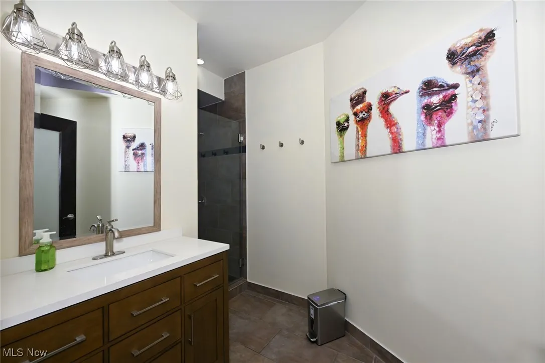 Bathroom with baseboards, a tile shower, tile patterned flooring, and vanity
