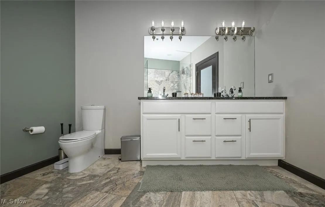 Bathroom featuring baseboards, toilet, walk in shower, and vanity
