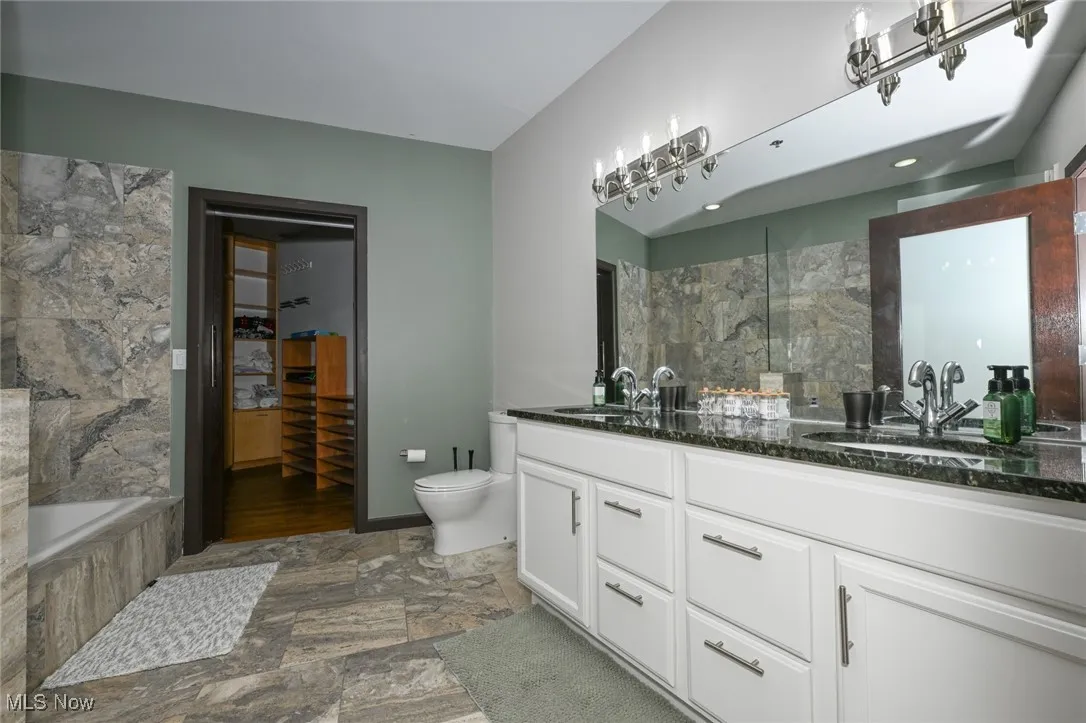 Bathroom with double vanity, a sink, toilet, and stone finish flooring